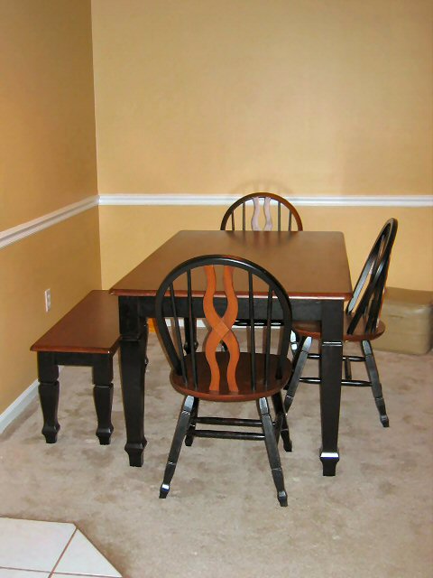 1985 Ford LTD Crown Victoria - A dining set with a dark wood table, black chairs, and a bench is arranged on a carpeted floor.