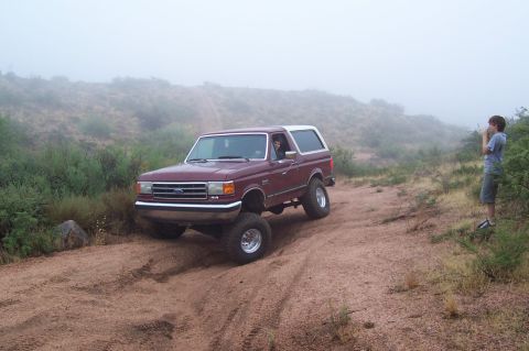 1992 Ford Bronco - A maroon 1992 Ford Bronco with a white top navigates a dusty, off-road trail.
