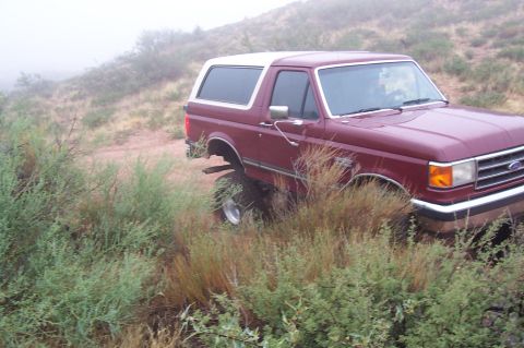 1992 Ford Bronco - Maroon 1992 Ford Bronco parked on a dirt path with brush and fog in the background.