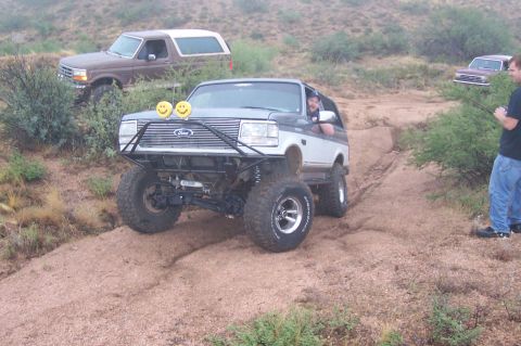 1992 Ford Bronco - A modified 1992 Ford Bronco navigates a dirt trail with other vehicles in the background.