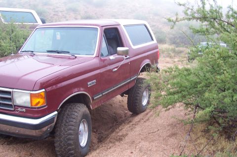 1992 Ford Bronco - Maroon 1992 Ford Bronco on a dirt trail with a white SUV in the background.