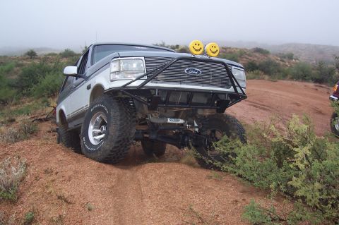 1992 Ford Bronco - This modified Ford Bronco is navigating a dusty, off-road trail with another vehicle visible in the background.