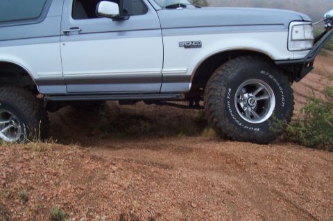 1992 Ford Bronco - A 1992 Ford Bronco with off-road tires navigates a dirt path.