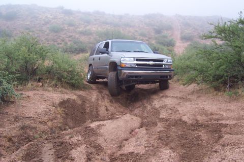 1992 Ford Bronco - This silver SUV navigates a challenging off-road terrain with steep inclines and loose dirt.