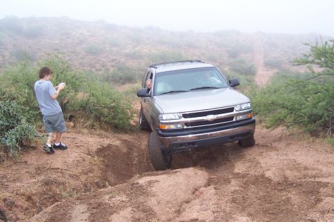 1992 Ford Bronco - A silver Chevrolet Tahoe navigates a challenging off-road terrain with a person photographing the scene.