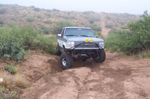 1992 Ford Bronco - A lifted 1992 Ford Bronco navigates a rough, dusty trail in a dry, brushy landscape.