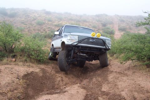 1992 Ford Bronco - This modified Ford Bronco is navigating a steep, dusty trail in a dry, scrubby environment.