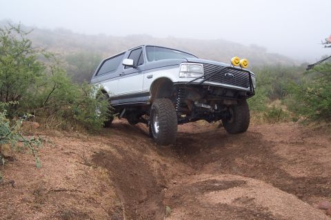 1992 Ford Bronco - A modified Ford Bronco navigates a challenging off-road trail in foggy conditions.