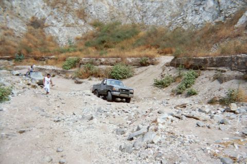1990 Ford Bronco - dark pickup truck sits in a rocky dry wash while a person in white stands off to the left in the canyon.