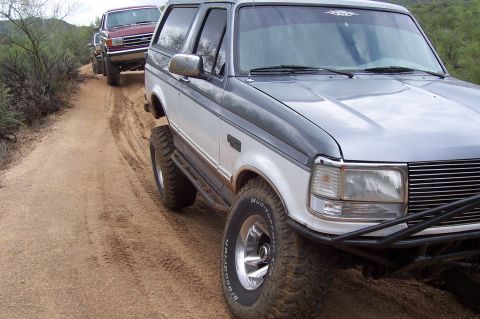 1992 Ford Bronco - Two Ford Broncos navigate a dusty trail in a rural landscape.