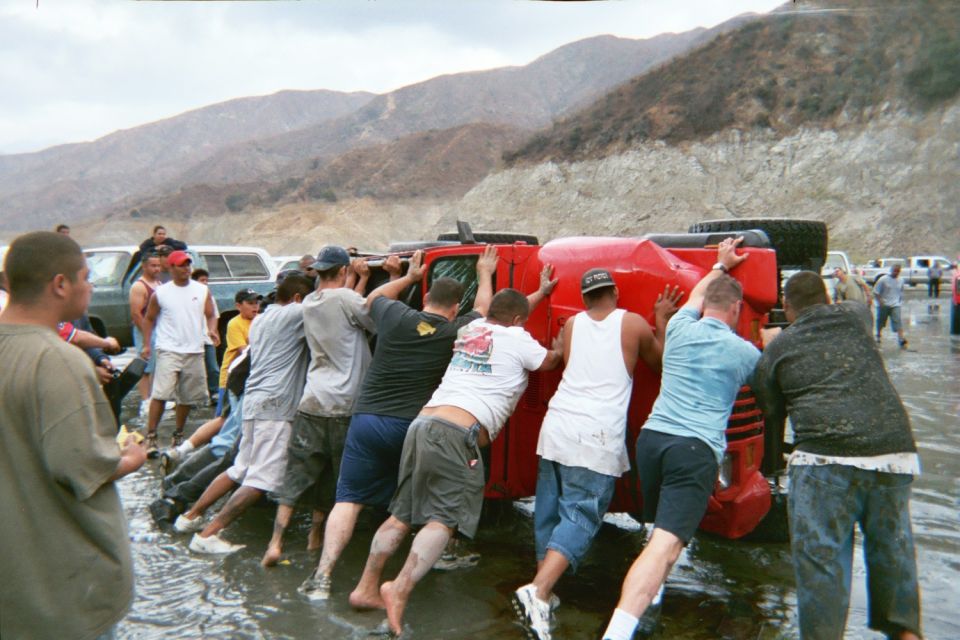 Group of people pushing an overturned red Jeep to right it in shallow water