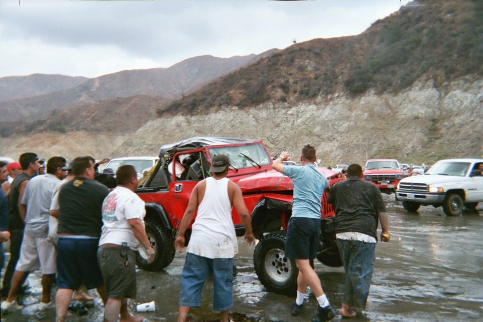 Red Jeep being pushed upright in muddy water with crowd and trucks around