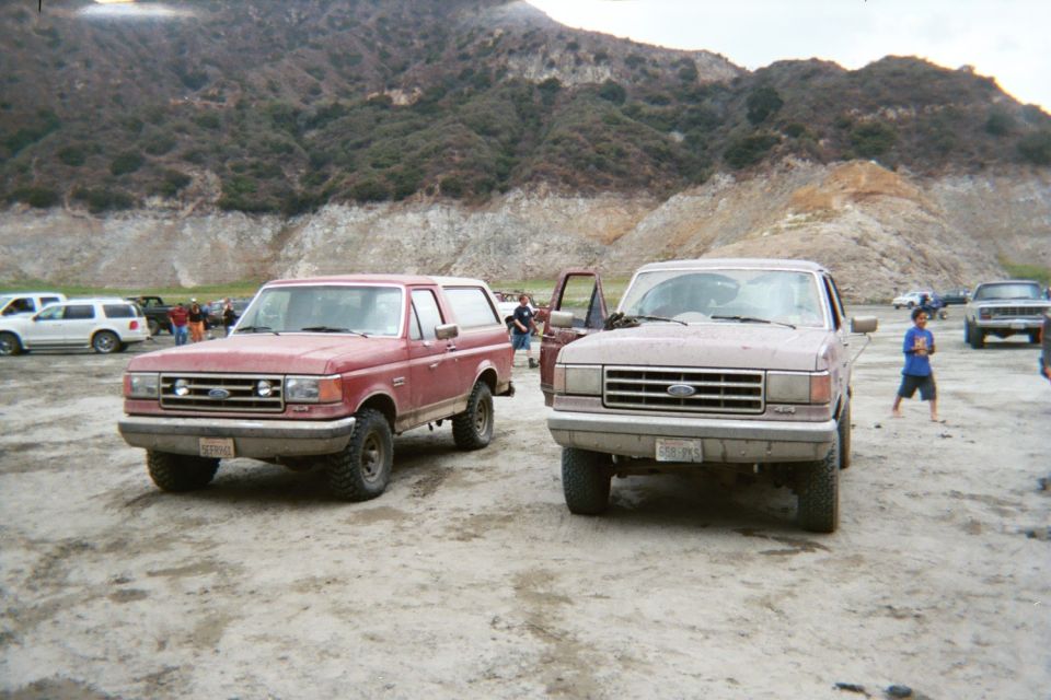 Red Ford Bronco and red Ford pickup parked side by side on dirt at a quarry