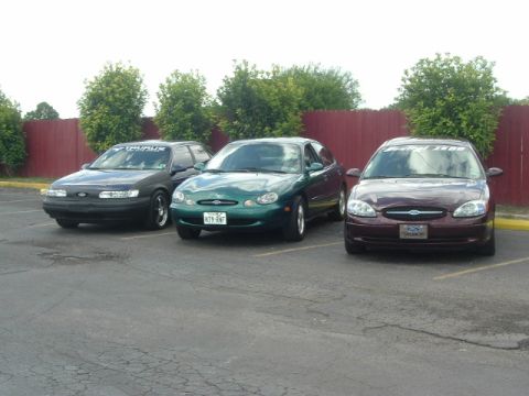 1993 Ford Taurus - A maroon 1996 Ford Taurus is parked in front of two other Taurus models in a parking lot.
