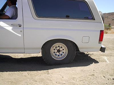 1990 Ford Bronco - close rear-quarter view of a white Ford Bronco highlights its chrome alloy wheel and off-road tire on sandy ground.