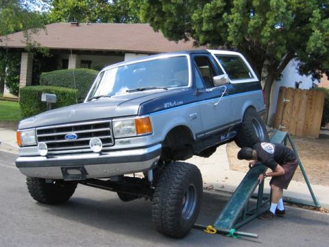 1989 Ford Bronco - A person works on a lifted Ford Bronco that is positioned on green metal ramps.