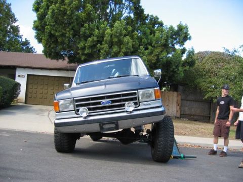 1989 Ford Bronco - A lifted Ford Bronco is propped up on a jack in front of a suburban garage.