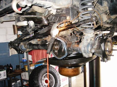 1985 Ford Bronco - This image shows the underside of a vehicle, focusing on the front axle, suspension, and steering components during maintenance.