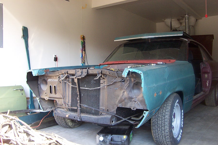 Teal coupe in garage with front end stripped, exposing radiator and frame during restoration