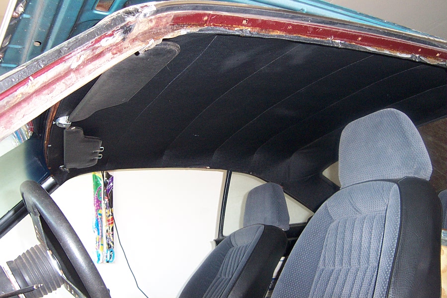Car interior showing headliner, seats, and steering wheel. Water damage is visible around the windshield frame