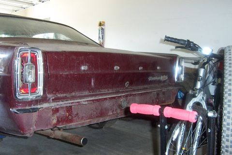 1966 Ford Fairlane - The rear of a maroon 1966 Ford Fairlane is parked next to a bicycle in a garage.