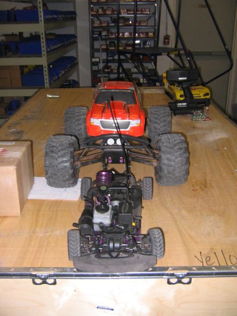 1994 Ford Bronco - Two remote control trucks are positioned on a wooden table, with shelves filled with items in the background.