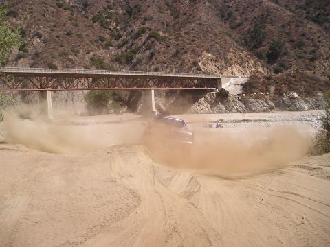 1989 Ford Bronco - Bronco driving through dust on a dirt road under a bridge.