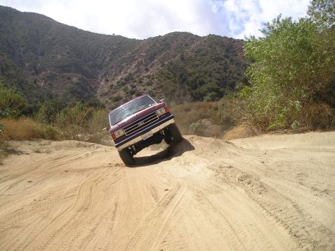 1989 Ford Bronco - This SUV is navigating a challenging off-road trail with steep inclines and loose dirt.