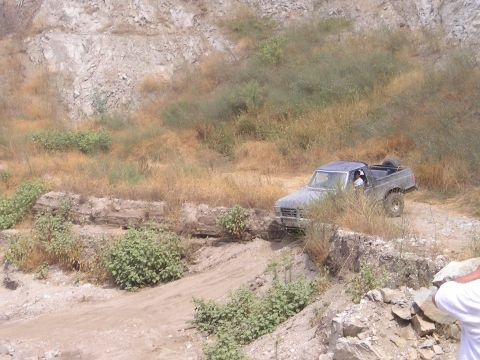 1989 Ford Bronco - A gray Ford Bronco navigates a rough dirt trail in a dry, hilly landscape.