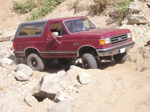 1989 Ford Bronco - 1989 Ford Bronco tackling a challenging rocky trail with its tires on uneven terrain.