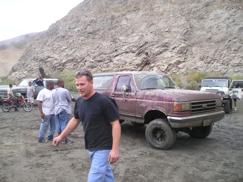 1989 Ford Bronco - A group of people and vehicles, including a maroon 1989 Ford Bronco, are gathered in a dusty, rocky area.