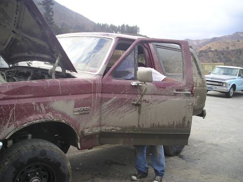 1989 Ford Bronco - This SUV is covered in mud, with its hood and driver's door open. Another vehicle is visible in the background.