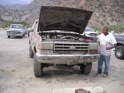1989 Ford Bronco - A dusty 1989 Ford Bronco sits with its hood open, a man stands beside it, and other vehicles are visible in the background.