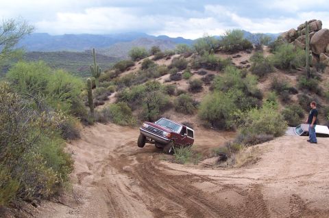 1992 Ford Bronco - A 1992 Ford Bronco navigates a steep, dusty trail in a desert landscape with cacti and mountains in the background.