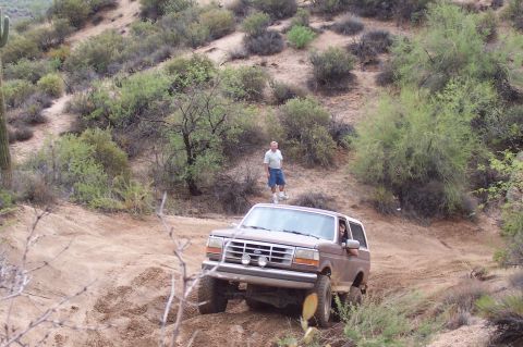 1992 Ford Bronco - A 1992 Ford Bronco navigates a dusty, arid terrain with a man observing from a hillside.
