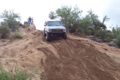 1992 Ford Bronco - A silver 1992 Ford Bronco navigates a steep dirt incline in a desert landscape.