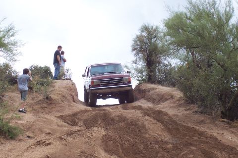 1992 Ford Bronco - Maroon lifted Ford Bronco crawling down a steep rutted dirt hill on oversized mud-terrain tires, front bumper and grille facing the camera…
