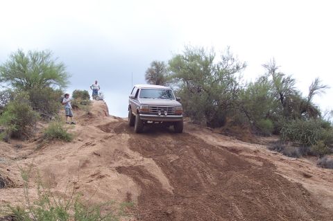 1992 Ford Bronco - A brown 1992 Ford Bronco navigates a steep dirt incline in a desert landscape.