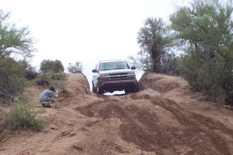 1992 Ford Bronco - A person photographs an SUV navigating a challenging dirt incline in a dry, brushy landscape.