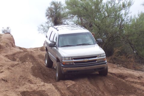 1992 Ford Bronco - Silver SUV navigates a sandy incline with sparse desert vegetation.