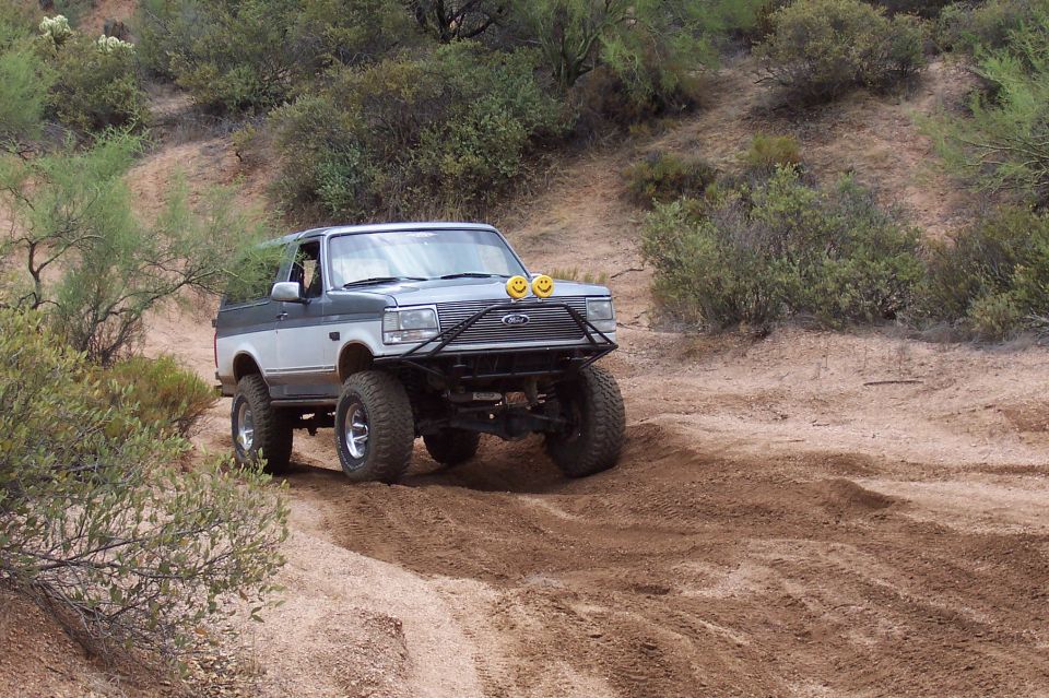 1992 Ford Bronco on dirt road, two-tone paint, off-road tires, custom bumper