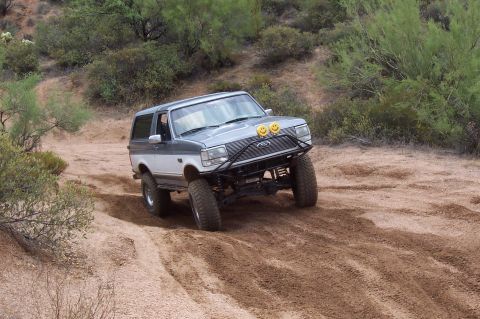 1992 Ford Bronco - This modified Ford Bronco navigates a dusty, off-road path with desert vegetation in the background.