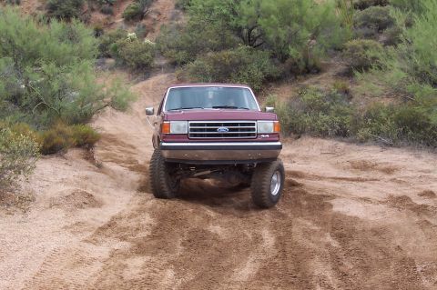 1992 Ford Bronco - This lifted Ford F-Series truck navigates a sandy, off-road path with desert vegetation in the background.