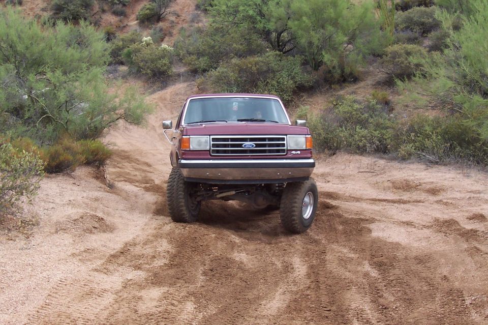 Maroon Ford F-Series truck with lifted suspension driving on a dirt trail