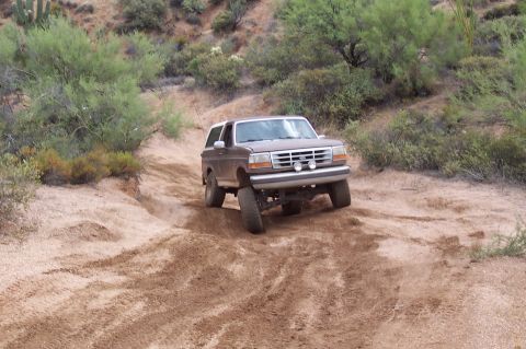1992 Ford Bronco - A brown 1992 Ford Bronco navigates a dusty, off-road trail with sparse desert vegetation.