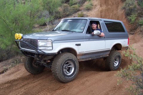 1992 Ford Bronco - A man drives a lifted 1992 Ford Bronco on a dusty, off-road trail.
