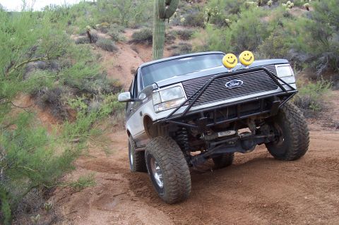 1992 Ford Bronco - A 1992 Ford Bronco navigates a desert trail with large tires and a custom front bumper.