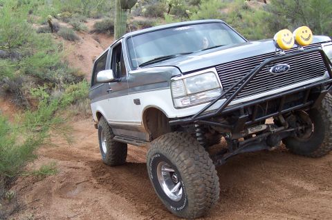 1992 Ford Bronco - This lifted 1992 Ford Bronco features a custom front bumper and off-road tires, seen navigating a dusty trail.