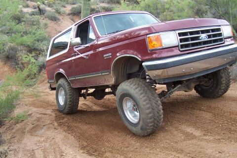 1992 Ford Bronco - This lifted Ford Bronco navigates a dusty, off-road trail with cacti and brush in the background.