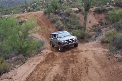 1992 Ford Bronco - Silver Chevrolet Tahoe navigates a steep dirt trail in a desert landscape.